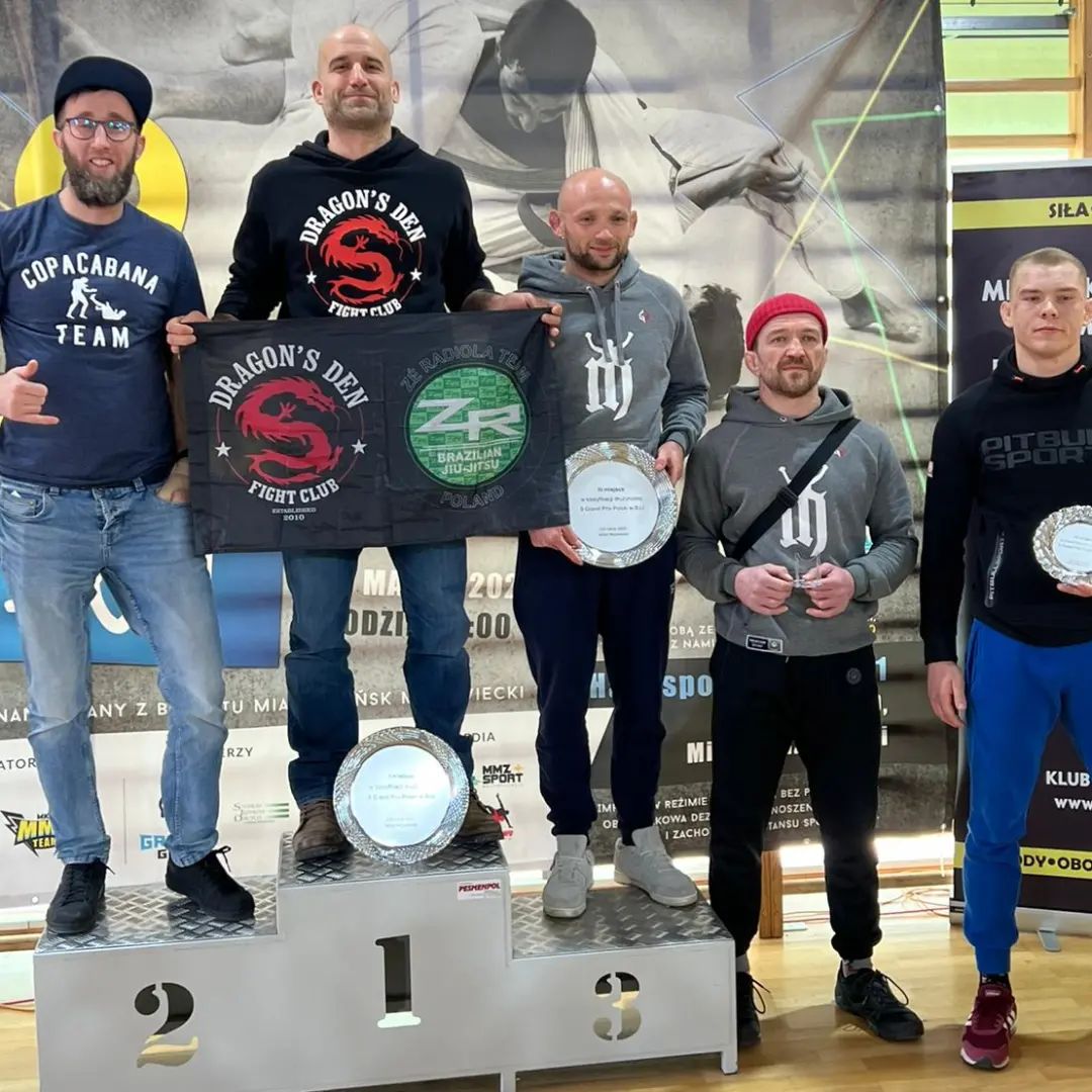BJJ team seating at the platform holding medals and trophies