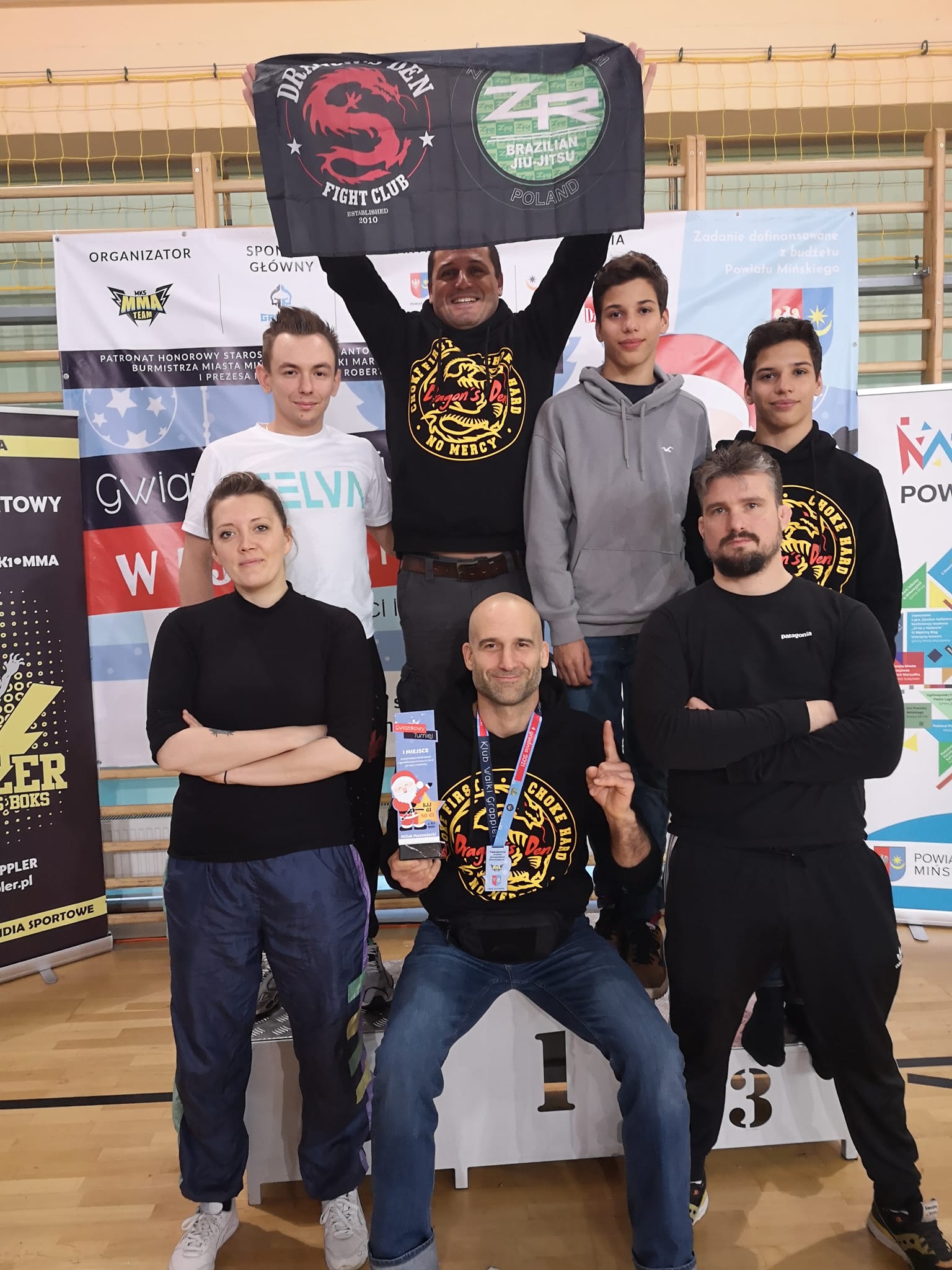 BJJ team seating at the platform holding medals and trophies